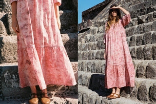 Woman in a pink dress standing on stone steps with a clear blue sky.