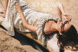 Woman lying on sand wearing a floral dress with 'Sunflower Silks' text overlay.