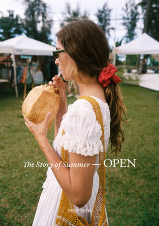 Woman in a white dress with yellow accents holding a coconut, with text overlay 'Summer Chapter I — OPEN' and 'SHOP NOW'.