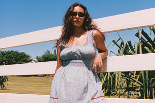 Woman leaning on fence in a blue floral dress and black sunglasses