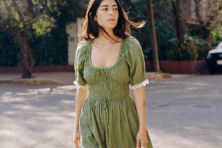 Woman in a green dress standing outdoors with trees and a car in the background