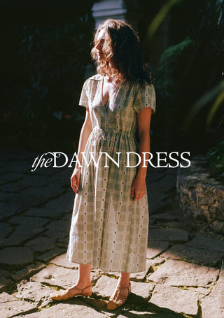 Woman wearing a patterned dress standing on a stone path with 'the DAWN DRESS' text overlay.