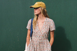 Woman wearing a floral dress and yellow cap against a green wall