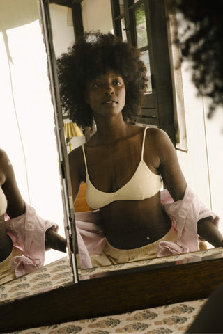 Woman in a white bra standing in front of a mirror with a pink garment on.