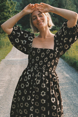Woman in a black floral dress standing on a path with greenery around