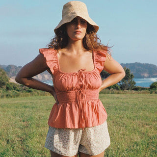 Woman wearing a pink top and beige hat in a grassy field with a scenic background