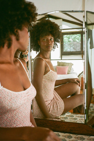 Woman in a pink slip dress sitting in front of a mirror in a bedroom.