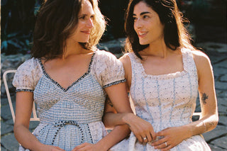 Two women sitting outdoors wearing matching dresses.