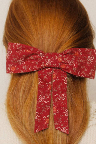 Red ribbon and floral hair bow on a person's head with a plain background