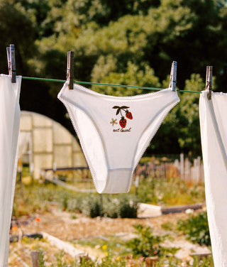 White underwear with a cherry design hanging on a clothesline outdoors.