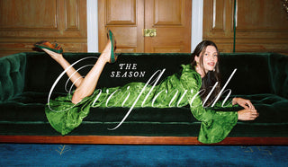 A woman reclining on a dark green velvet sofa in front of wooden doors, wearing a shiny green satin-like dress and green shoes. Large white script text overlays the center of the image.