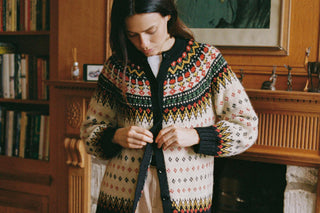 Woman wearing a patterned sweater in a room with bookshelves and a fireplace.