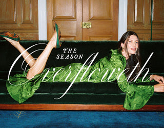 A woman reclines on a dark green velvet sofa in front of wooden doors, wearing a green patterned dress and green pointed shoes. Large white script text overlays the center of the photo.