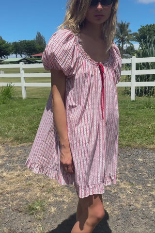 A video of a woman in a red and white striped pattern dress standing in grass with a white fence in the background.