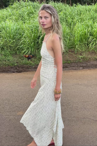 A woman wearing a white patterned backless dress, walking along a grassy road