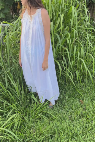 Woman in a white dress standing in a grassy field with greenery in the background