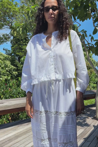 Woman wearing sunglasses and a white shirt outdoors with greenery in the background