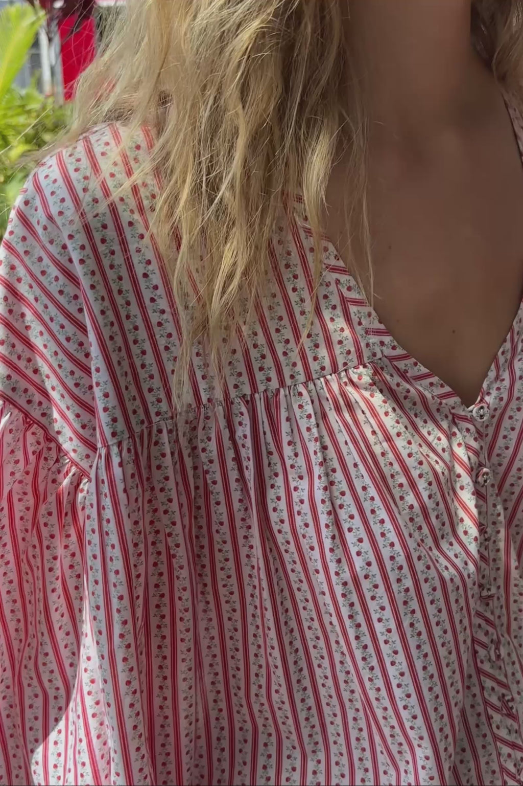 A video of a woman in a red and white striped outfit standing outside a shop.