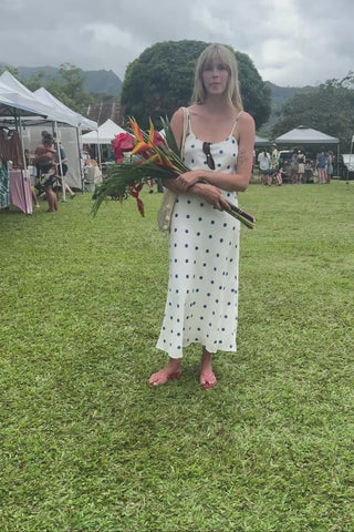 Woman in a polka dot dress holding tropical flowers at an outdoor market.