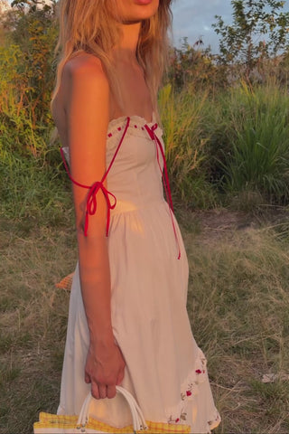 Video of a woman wearing a white dress with red accents and greenery in the background