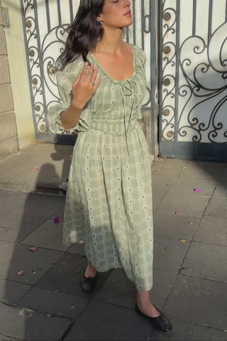 Woman in a green floral and plaid dress standing on a street 