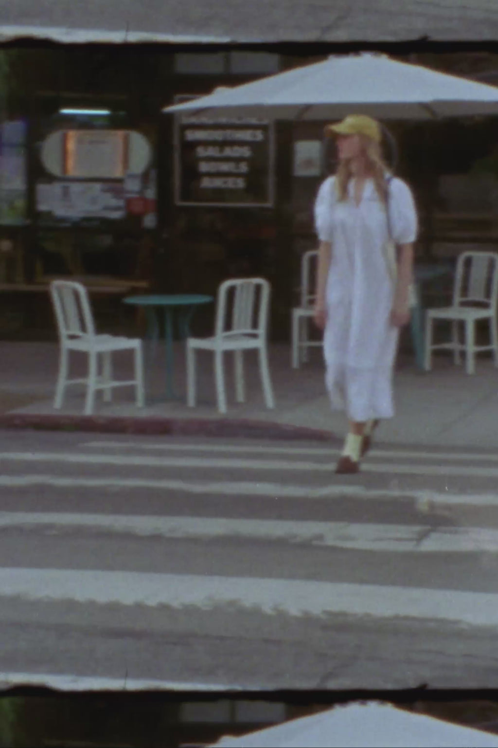 Woman walking across a street with a lace white dress and yellow cap