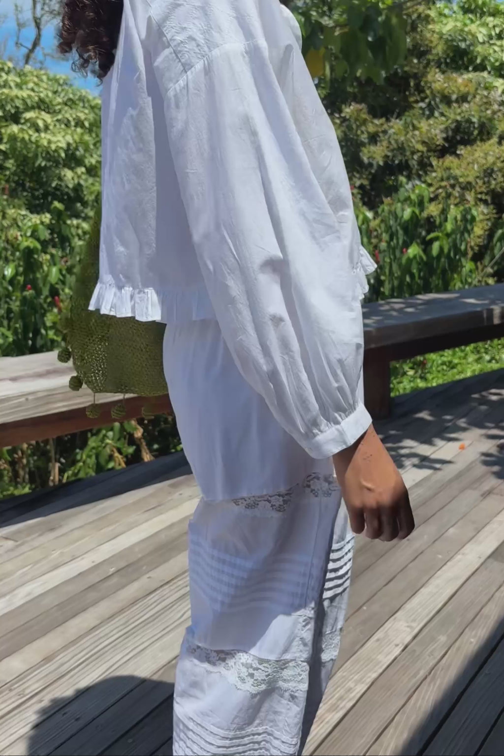 Woman in a white outfit walking on a road with greenery in the background