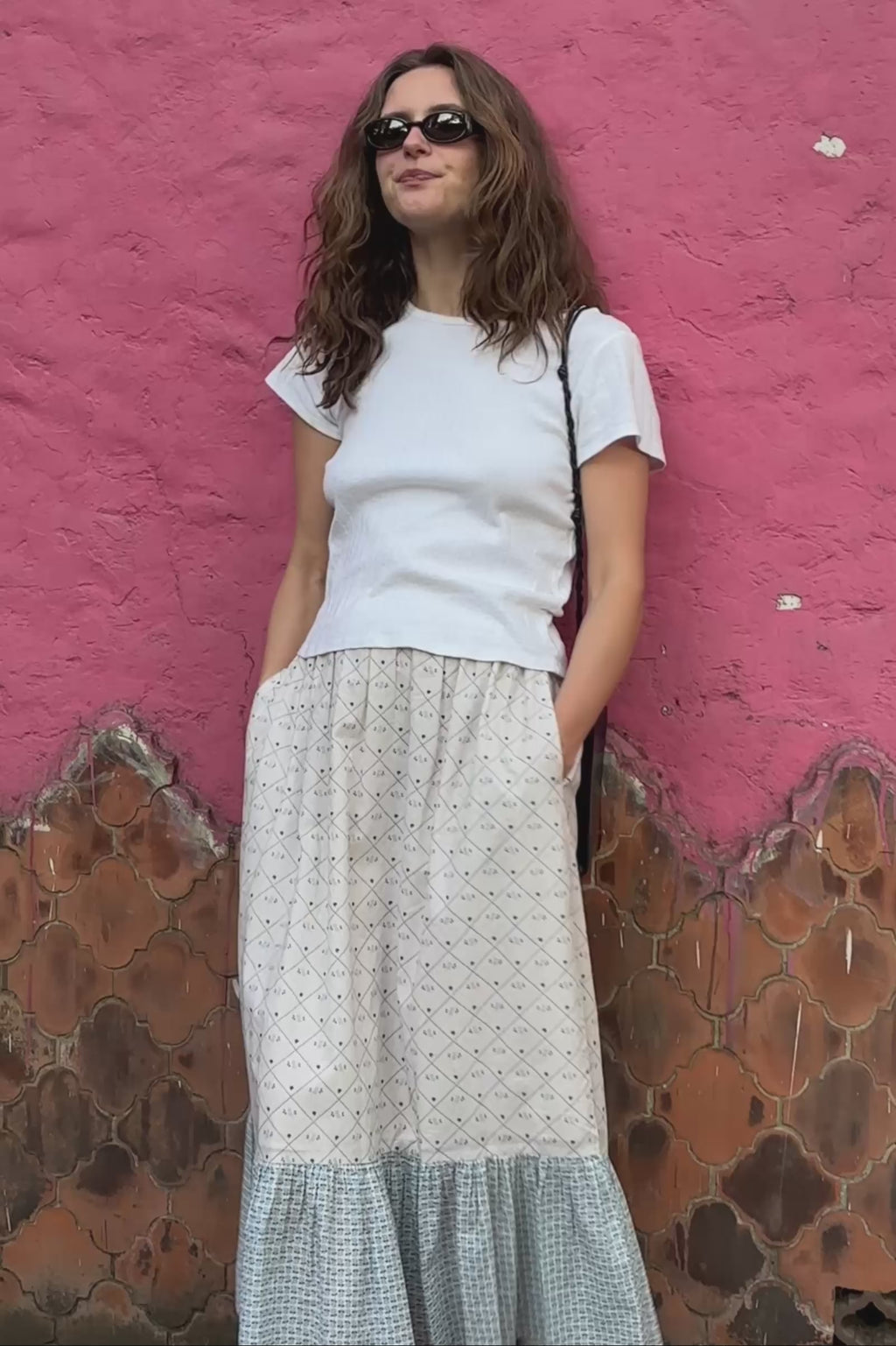Woman wearing a white top and blue checkered skirt against a pink wall.