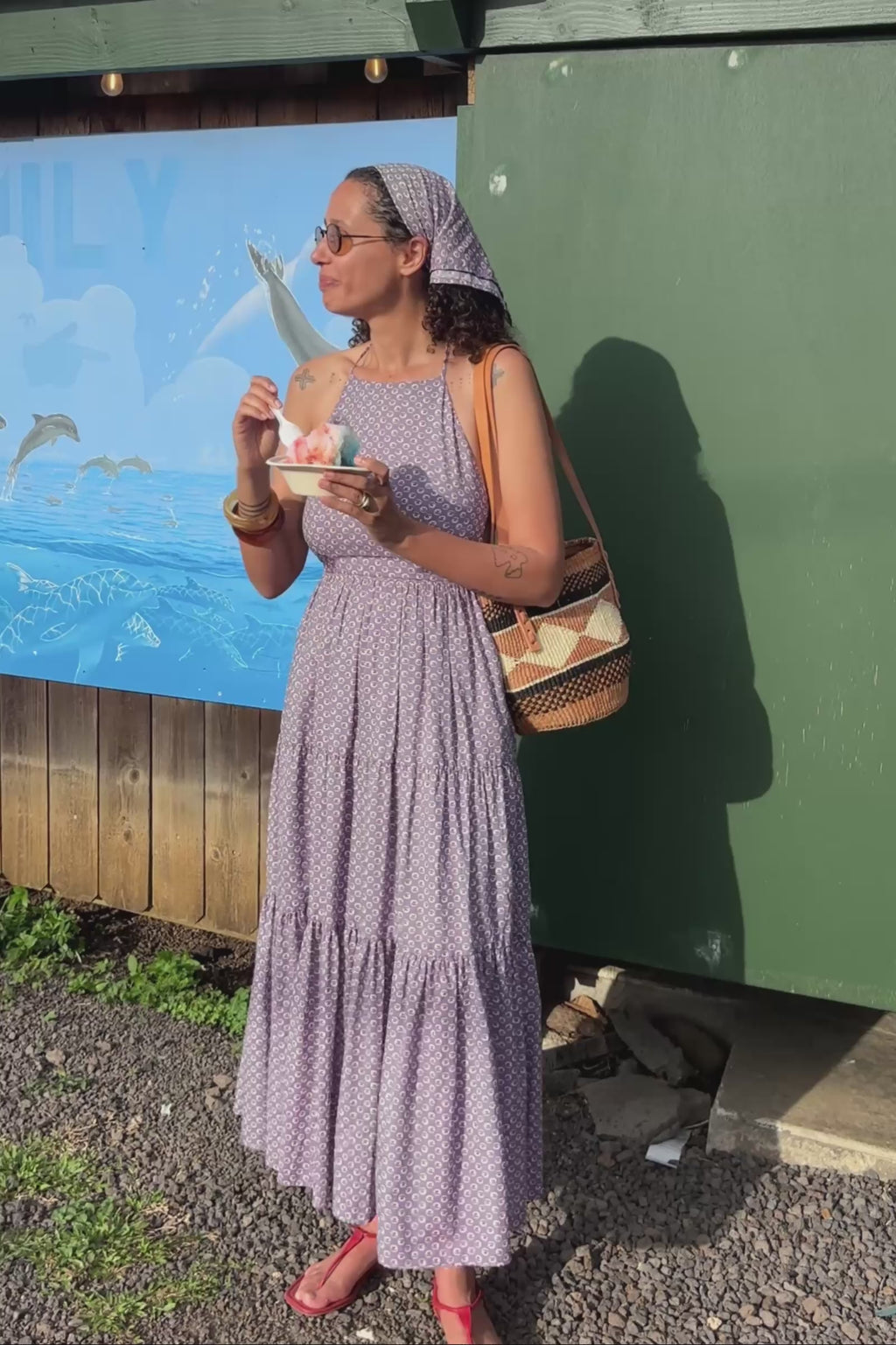 Woman in a purple dress standing under a 'Wishing Well' sign with a mural in the background.