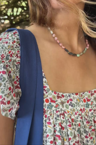 Woman in a floral dress walking on a dirt path with trees and a car in the background