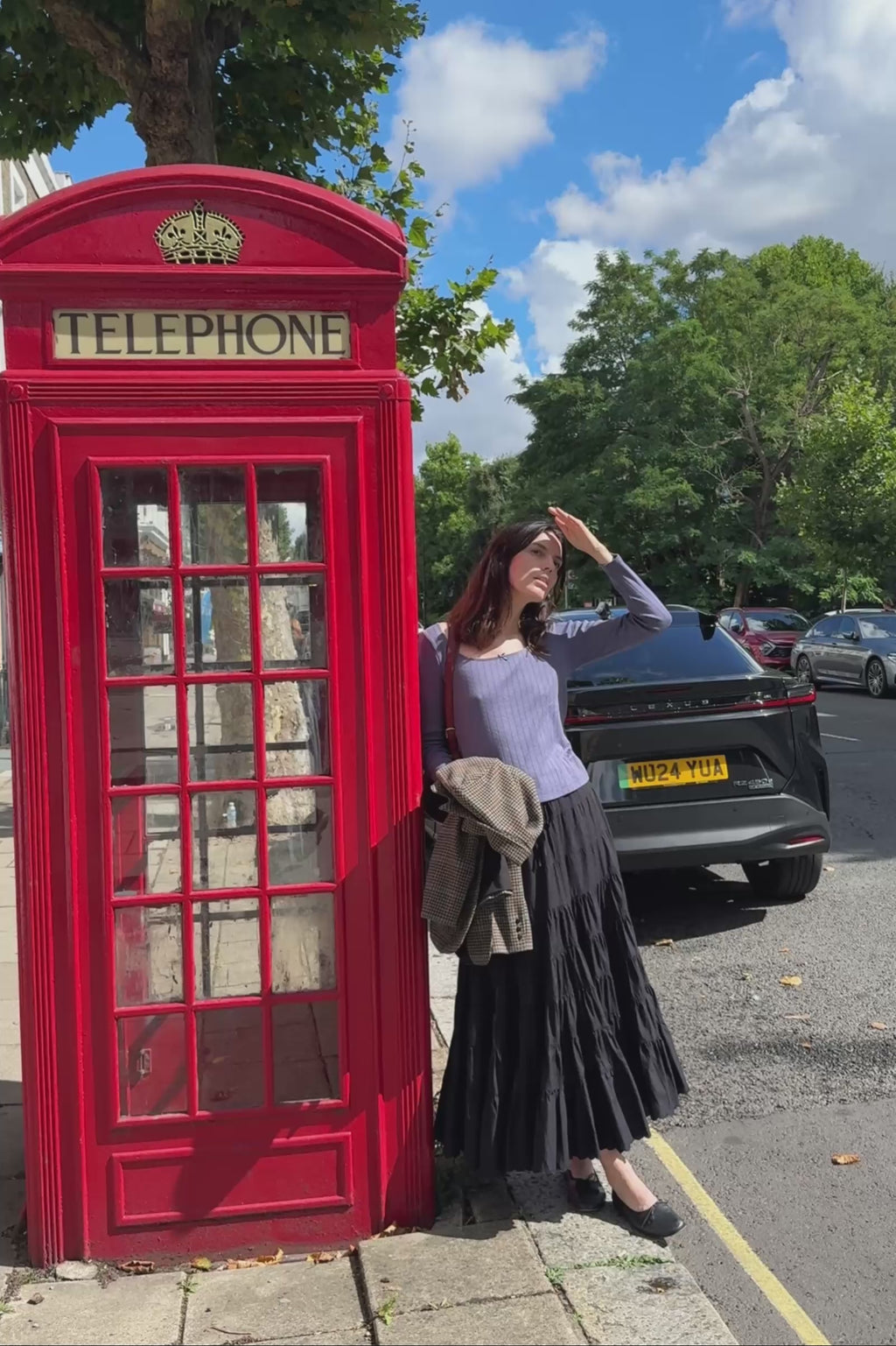 Woman in a blue scoop tee standing in front of a red telephone box 