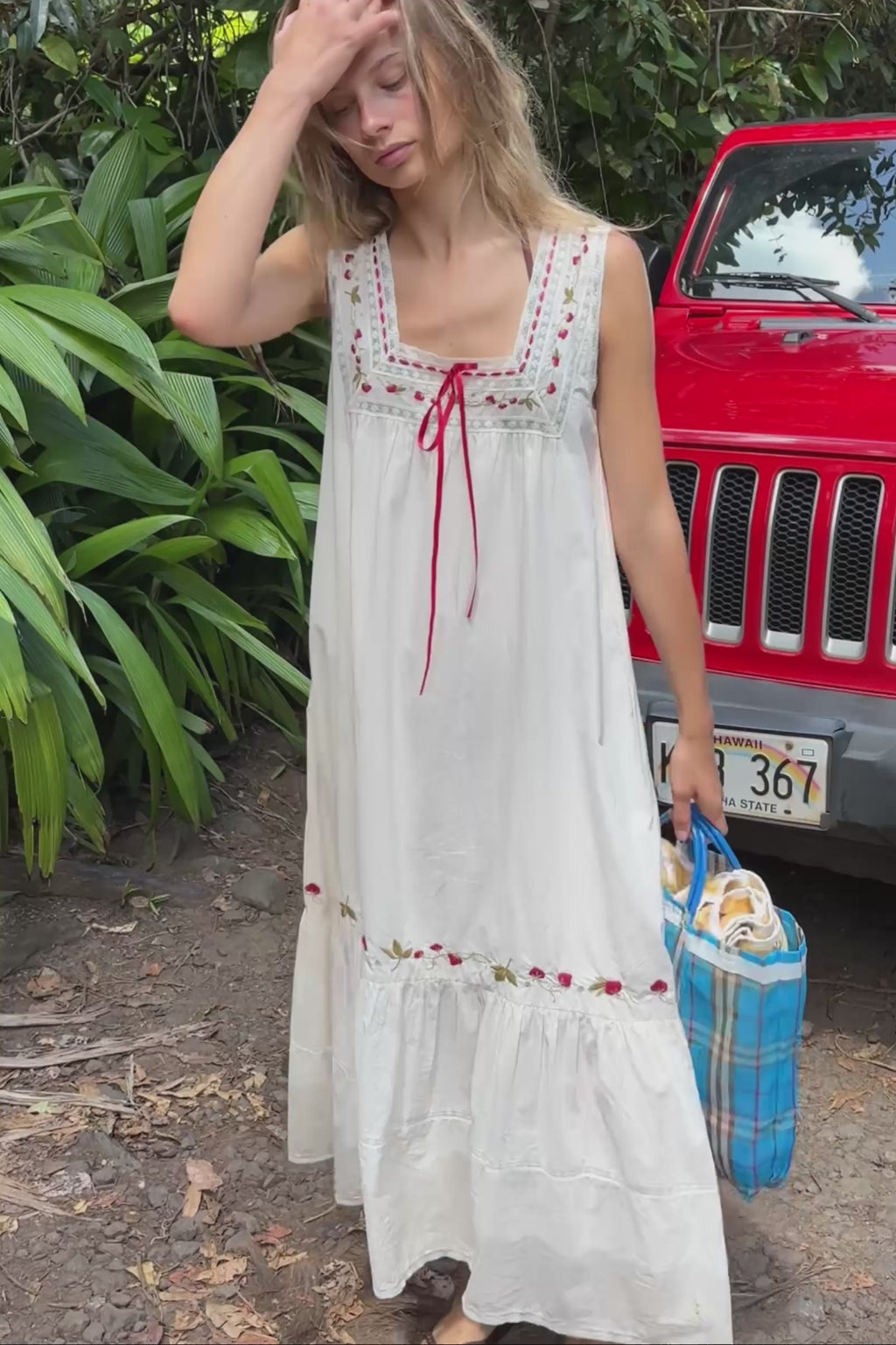 Video of a woman wearing a white lace and red embroidered dress, with close up of the details at the neckline.