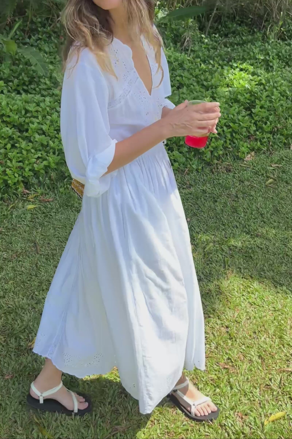 Woman in a white dress holding a yellow bag and drinking from a cup outdoors
