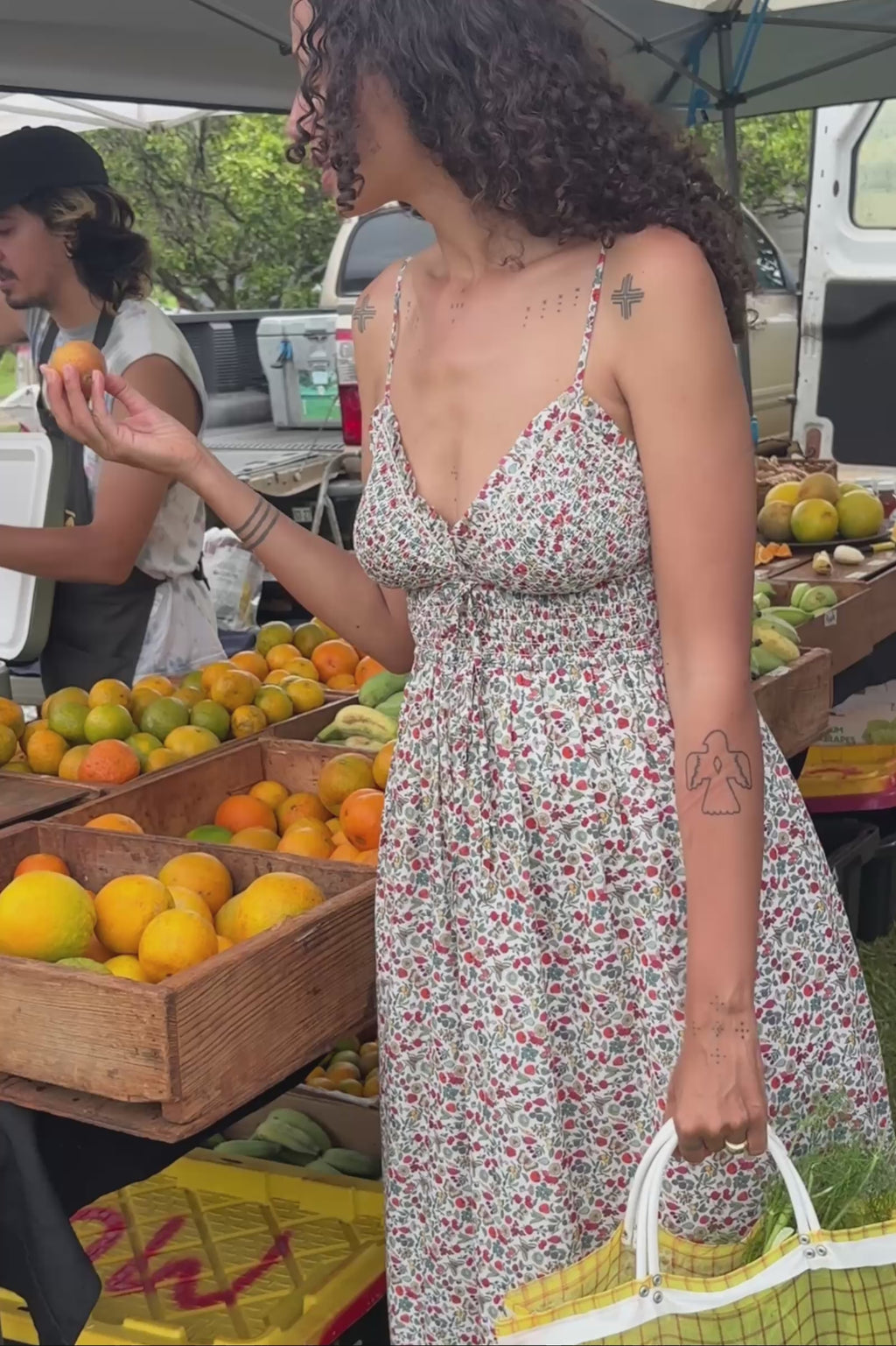 Woman holding a yellow fruit and vegetables with a yellow bag at an outdoor market.