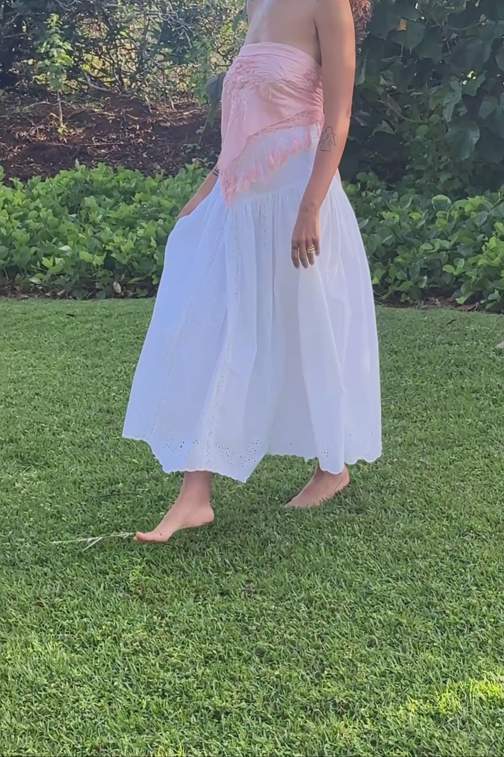 Person wearing a white skirt with a pink top in a garden setting