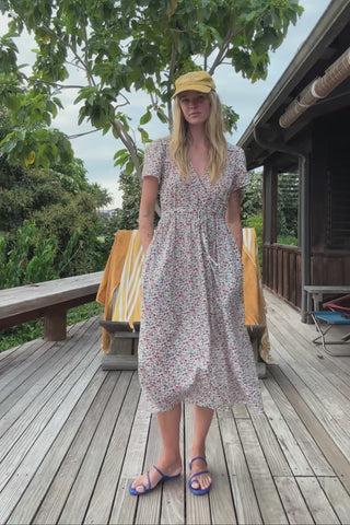 Woman in a floral dress and cap standing next to a green structure.
