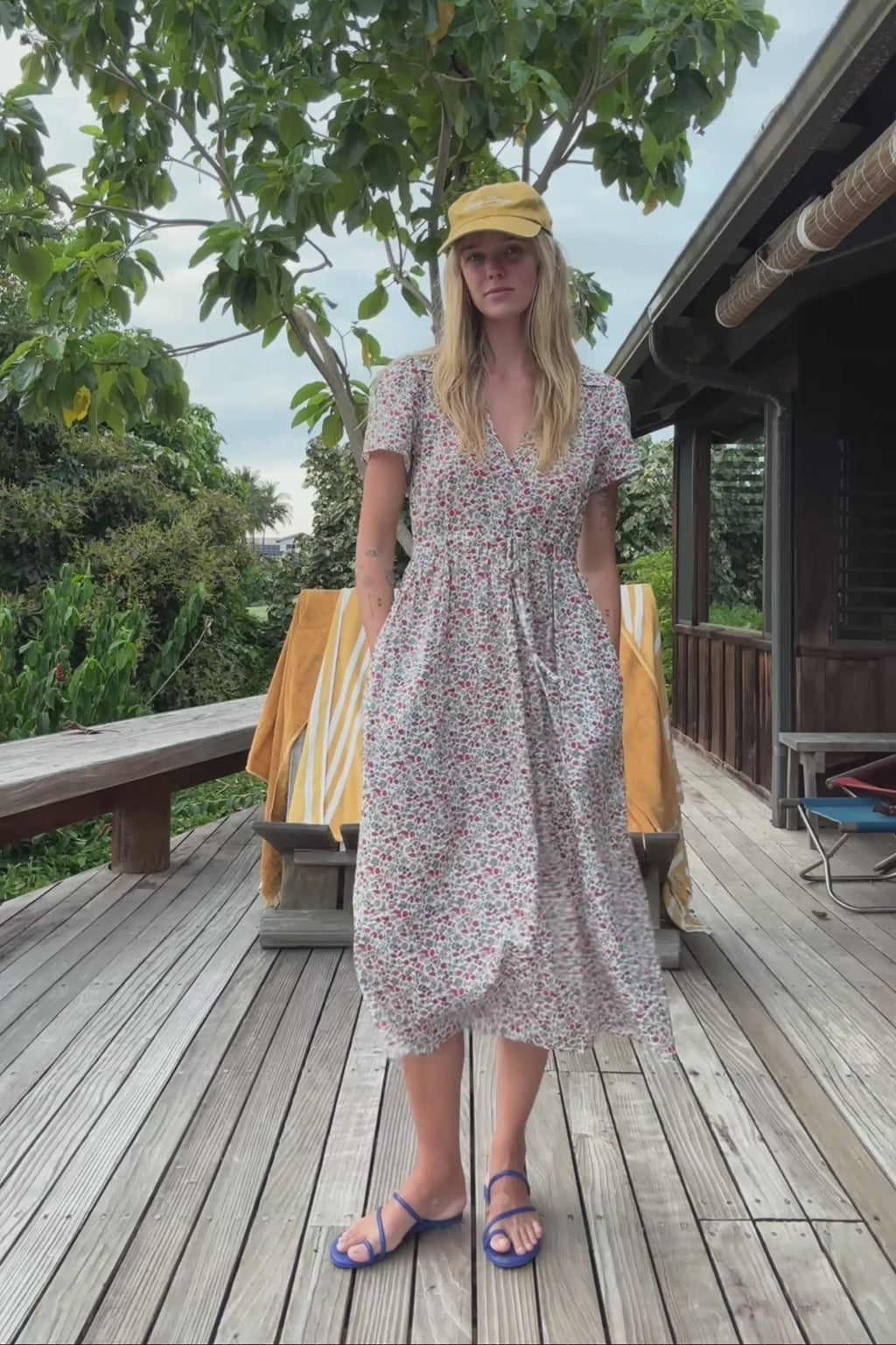 Woman in a floral dress and cap standing next to a green structure.