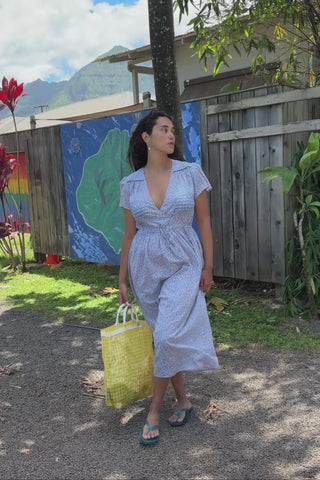 Video of a woman in a light blue floral patterned dress standing in front of a fence 