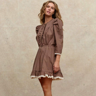 Woman wearing a brown polka dot dress with lace trim on a beige background